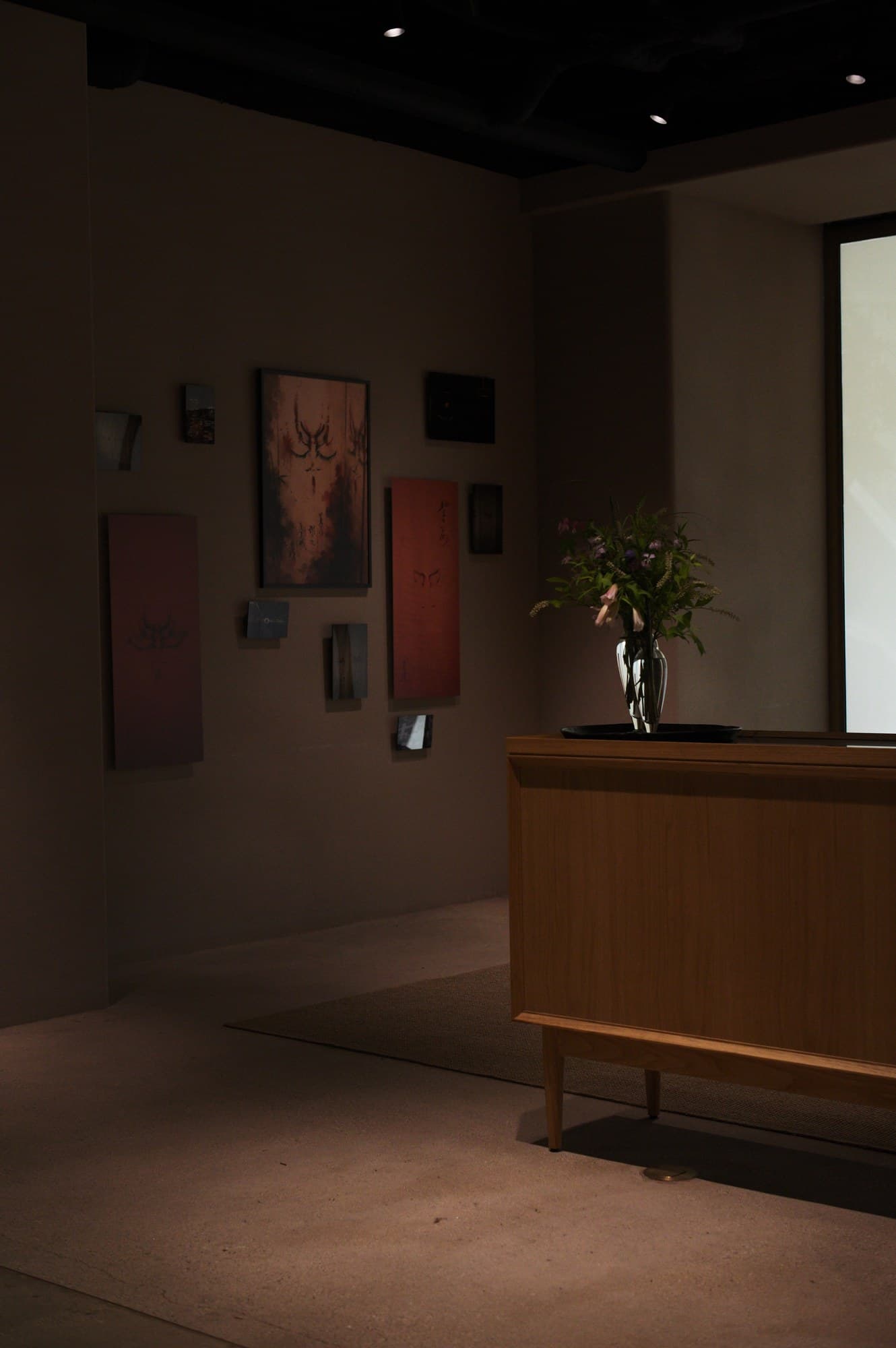 A corner of the room: works on red paper, with a flower-topped console in front