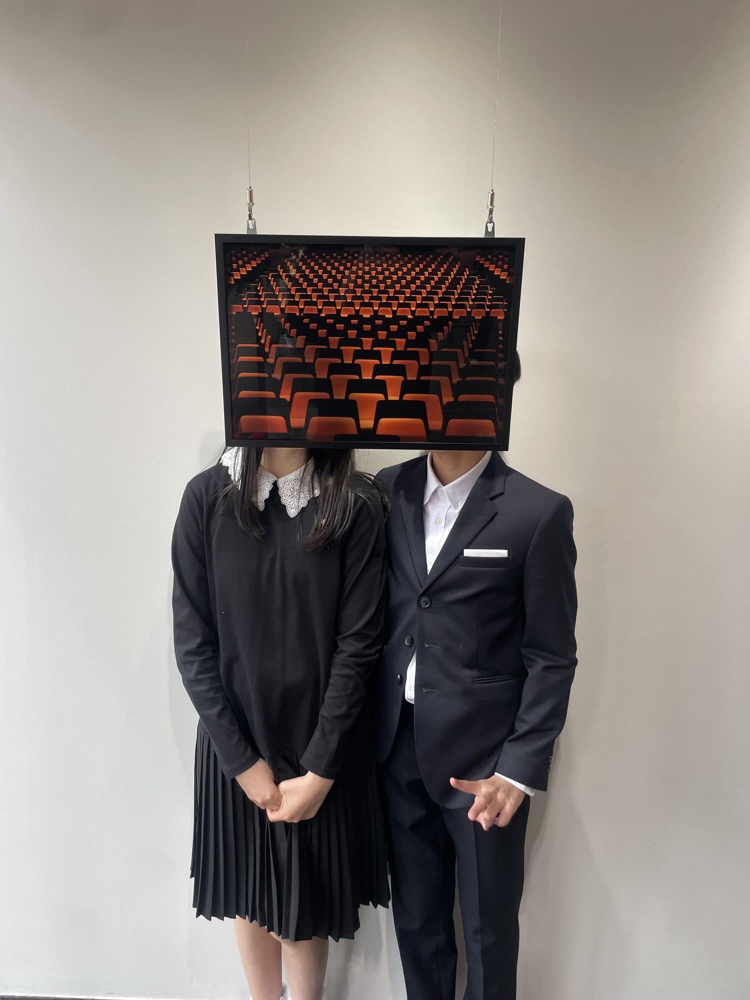 ワイヤーで吊られた客席の作品が、前に立つ二人の顔の位置にちょうど重なっている